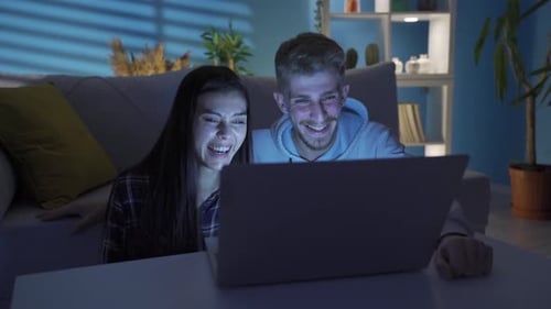 Smiling Couple Watching Laptop at Night at Home