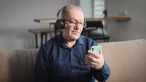 Un anciano jubilado escucha música con auriculares inalámbricos, entretenimiento en Internet para mayores