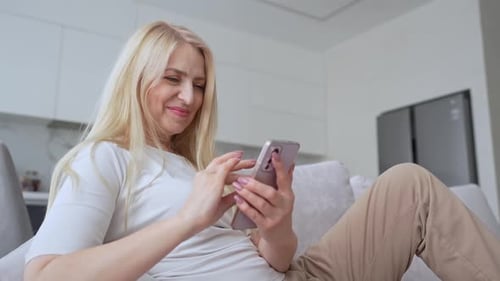 Woman Using Smartphone Relaxing on Couch at Home