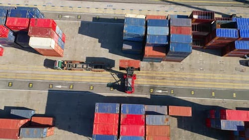 Vista de cima, uma empilhadeira descarregando contêineres de um caminhão em um terminal de contêineres em