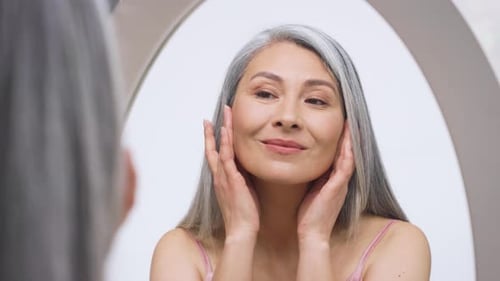 Woman in mirror touches face and smiles