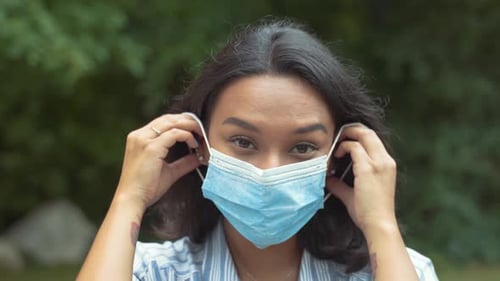 Woman Puts on a Surgical Mask in Nature