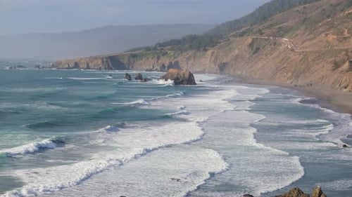 Aerial tracking showing Highway 1 winding along cliffs with waves crashing below