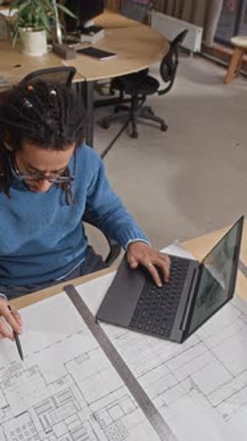 Architect Using Laptop while Working on Paper Building Plan in Office