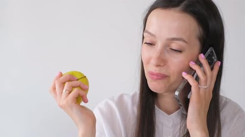 Portrait of a Businesswoman Talking on the Phone at Her Workplace in the Office and Eating an Apple