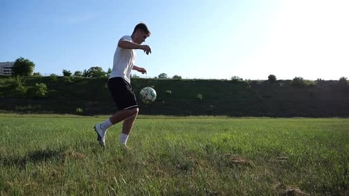 Sportler jongliert Fußball im Stadion bei Sunny Day Jongliert junger Mann kickt Ball auf der grünen Wiese