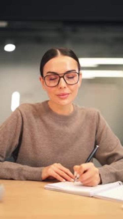 Joven sonriente escribiendo en cuaderno con gafas
