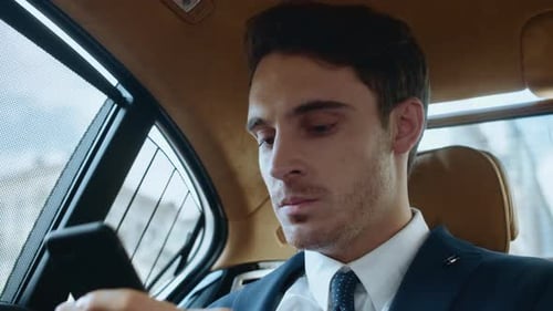 Young businessman using smartphone in luxury car