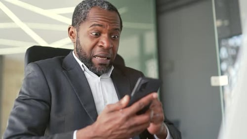 Close up. Happy mature african american man in formal suit receiving good news on smartphone while s