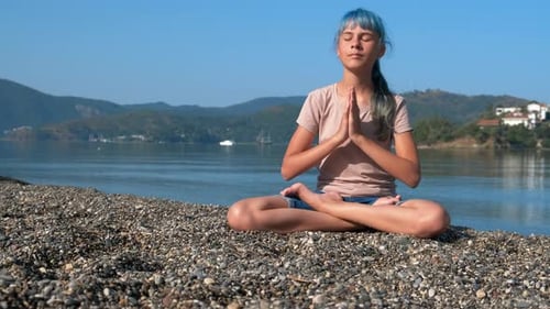 Teen Girl Meditating on Rocky Beach on Sunny Day