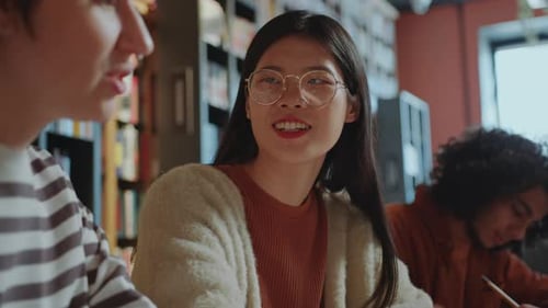 Fille asiatique parlant avec une camarade de groupe féminine à la bibliothèque