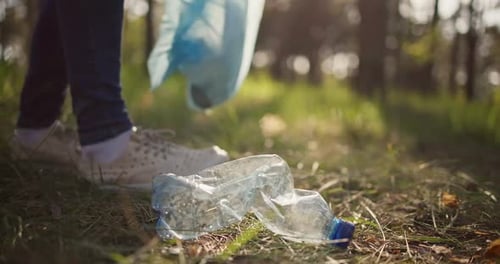 Woman Picking Up Trash Plastic Bottle Lying on the Ground in the Forest