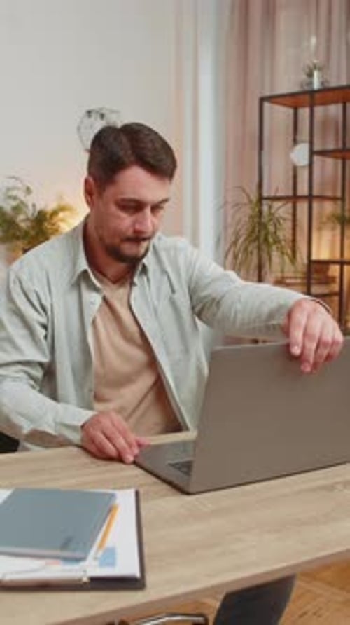 Caucasian Young Man Freelancer Opens Laptop and Working on Project Sitting at Home Office Table