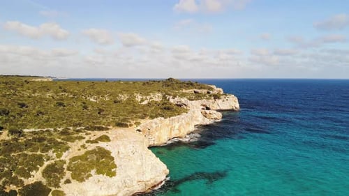 A forward panning shot showing the cliff line at the Cala Varques beach among a massive landscape an