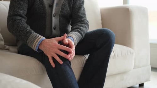 Man Massaging Sore Knee on Couch Indoors