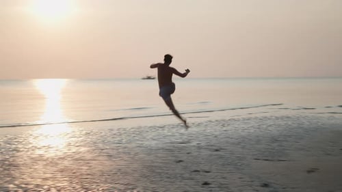 Young Man Running Barefoot on Beach at Sunrise