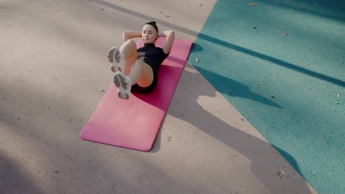Jeune femme effectuant des situps sur un tapis rose à l'extérieur