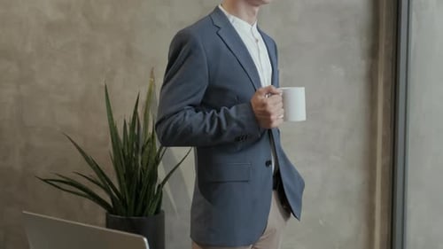 Elegant Businessman with Cup of Coffee STanding by Workplace in Home Office