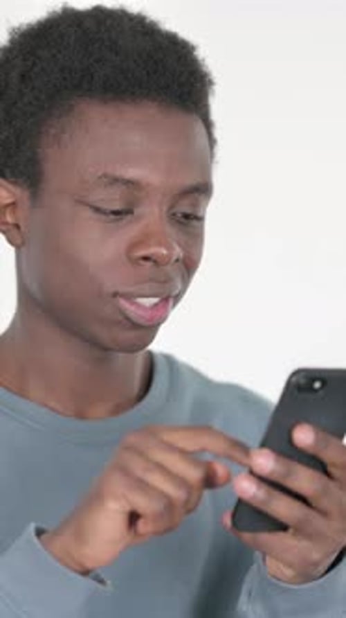 Young African Man Celebrating Success on Smartphone on White Background, Vertical Video
