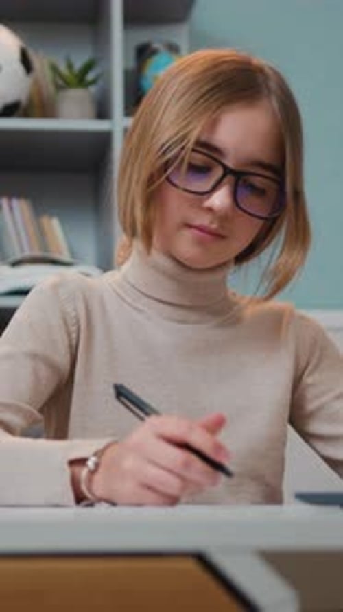 Girl with Glasses Writing at Desk Indoors