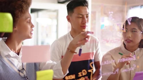 Felizes e diversificados colegas criativos masculinos e femininos discutindo ideias na parede de vidro, em câmera lenta