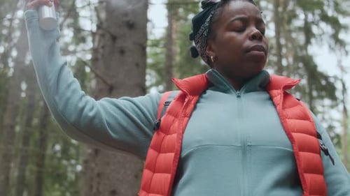 Black Woman Using Repellent Spray While Hiking in Forest