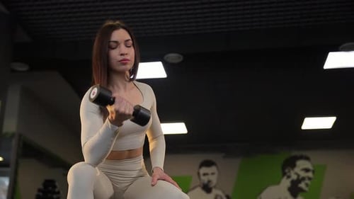 Sexy Young Brunette Lifting Dumbbell with One Hand in the Gym Active Training of a Young Woman
