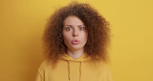 Surprised woman with curly hair against yellow backdrop