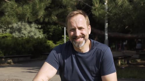 A Handsome Middleaged Caucasian Man Smiles at the Camera in a Park on a Sunny Day Ends in Closeup