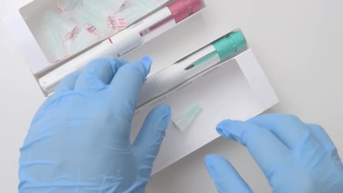 Blue gloved hands picking up a needle and a preloaded pen with more pens and medication injection co