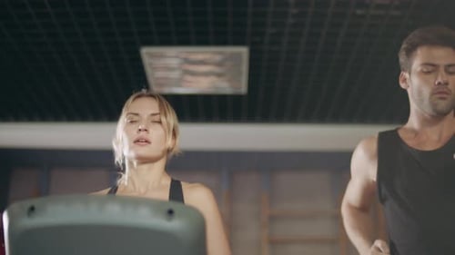 Concentrated Couple Running Together on Treadmill Machine in Gym Club. Beautiful Woman