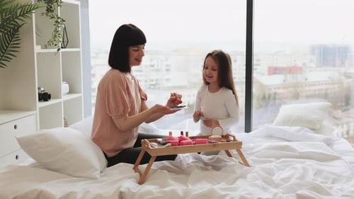 Une femme heureuse applique du maquillage avec un pinceau sur le visage d'une petite fille
