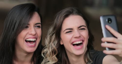 Friends taking selfie with cellphone. Authentic real life laugh of young women posing for photo
