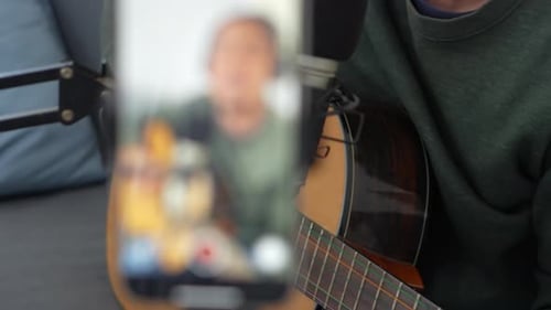 Man Playing Guitar While Recording with Phone