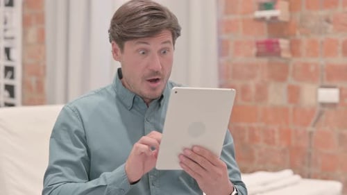 Man Celebrates Success with Tablet at Home