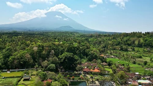 Drohnenaufnahme des Vulkans Mount Agung, der sich über Palmenwäldern und Reisfeldern in Ost-Bali, Indien, erhebt