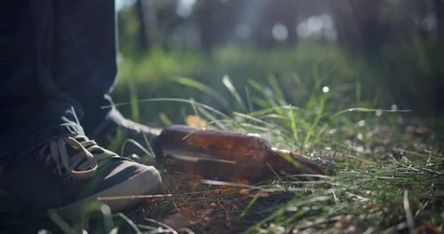 Un hombre con una bolsa de plástico recoge una botella de vidrio que está tirada en el césped mientras recoge basura en el