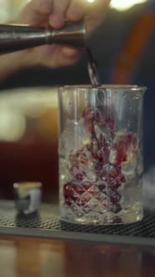 Un barman verse un verre d'alcool provenant d'un doseur dans un verre contenant de la glace pilée.
