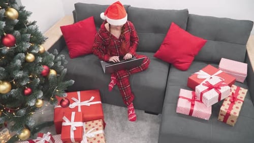 Woman Using Laptop with Christmas Gifts and Tree
