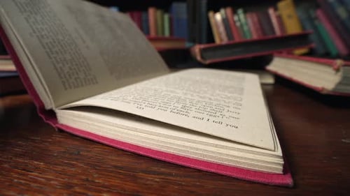 Slow motion view of book with red cover is closed shut on desk in library