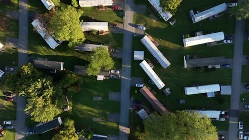 Dense populated mobile trailer homes with green grass in yards at sunset. American suburb