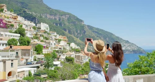 Two friends taking photos of the view using their smartphones while on holiday in Italy