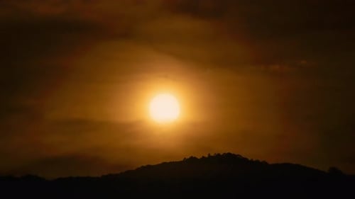 Time lapse of the sun setting over hills that are covered with clouds, in the style of smokey backgr