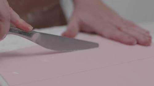 A person cuts lines carefully into pink ready rolled fondant icing