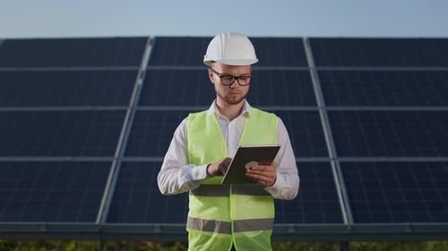 Engineer Standing on Farm with Solar Panels and Using Tablet
