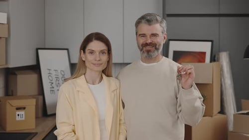 Portrait of Happy Couple Smiling Looking at Camera Holding House Key on the Carton Boxes Background