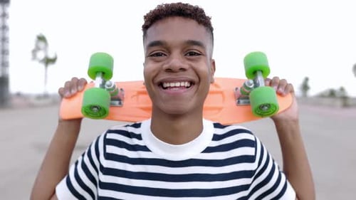 Smiling Young Adult Holding Skateboard on Urban Street