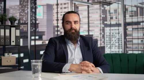 Bearded Man in Suit Sitting at Desk in Office