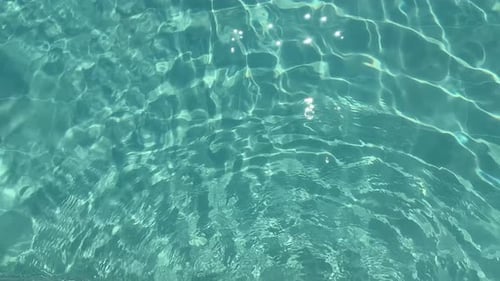 Blick von oben auf das klare blaue Poolwasser mit Sonnenreflexionen und sanften Wellen, erfrischend und