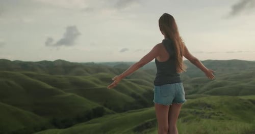 Woman with outstretched arms in grassy green hills